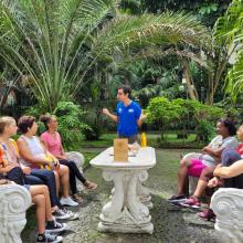 foto de alunos sentados em volta de uma mesa e um educador em pé conversando com eles